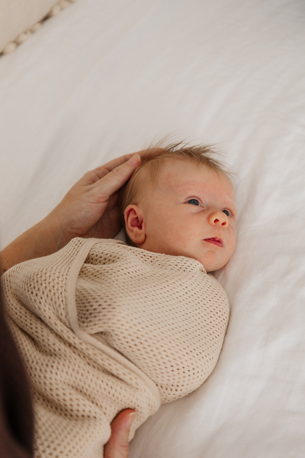 Newborn baby wrapped in a beige blanket on a white surface