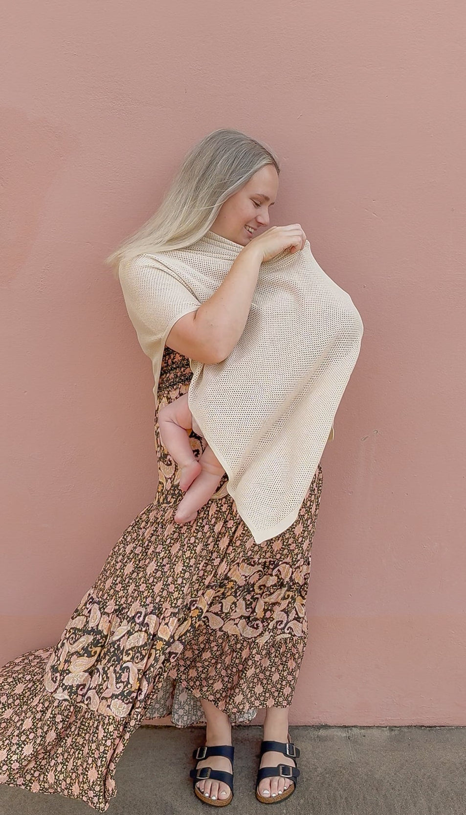 Woman breastfeeding  a baby  under the Cowrie nursing cover against a pink wall